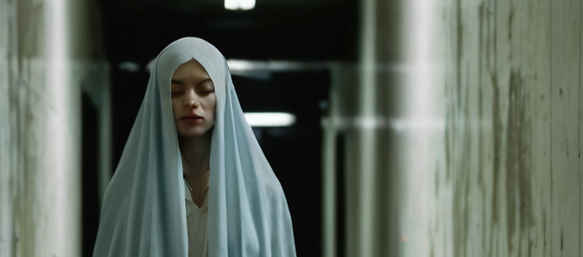 Recovered corridor still -- a veiled woman standing motionless in a fluorescent hallway